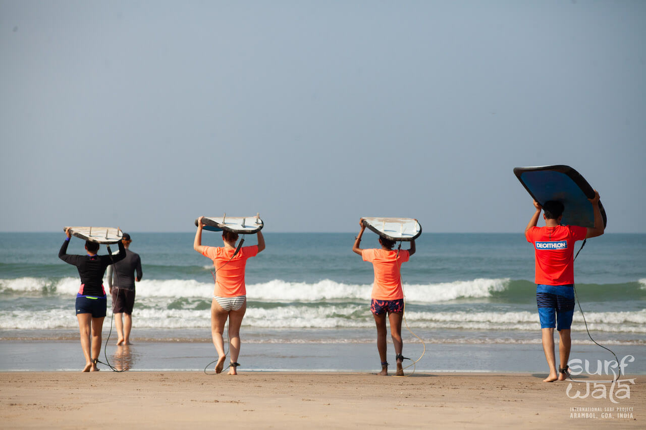 A group of guys and girls carrying surf boards head to the water to start surfing with their instructor leading the way